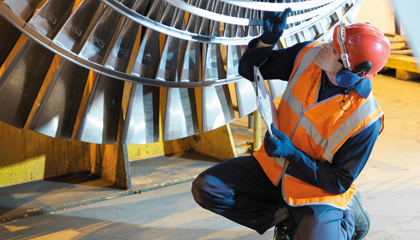 En man i skyddskläder och reflexväst inspekterar en maskinens säkerhet.